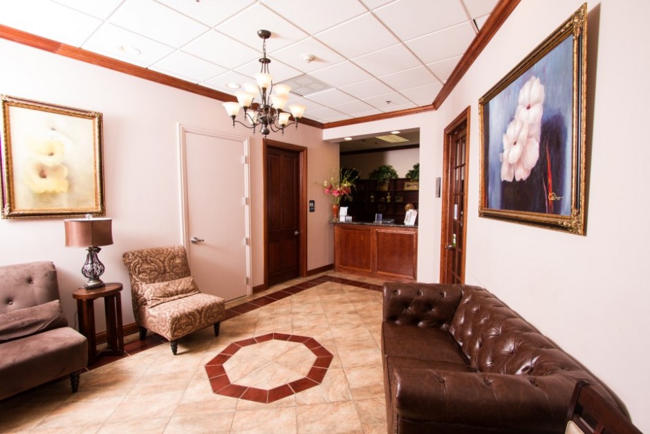 An interior view of a well-lit waiting room with a tiled floor, a brown leather couch, and a framed picture on the wall.