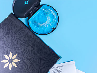 A blue toothbrush with a clear bristle head, placed on top of an open package that reads  DENTAL CRYSTALS  and has a black background with a white design resembling a flower or starburst pattern.