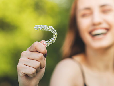 Smiling woman holding a transparent plastic retainer in her hand.