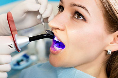 A woman receiving dental treatment, with a dental hygienist using an ultrasonic cleaning device and wearing protective gloves.