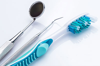 The image shows a collection of dental tools, including a toothbrush with blue bristles and a pair of scissors, arranged on a white surface.