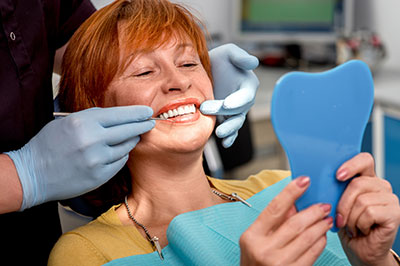 The image shows a woman in a dental chair, receiving dental treatment, with a dental professional working on her teeth.