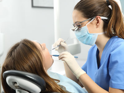 A dental hygienist is performing a cleaning on a seated patient s teeth, with both individuals wearing protective face masks.