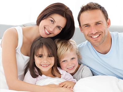 A family of four, including a man and woman with two children, posing for a photo in a bedroom setting.