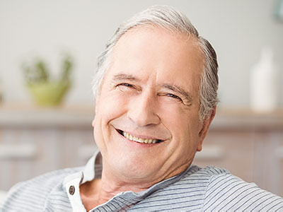 A smiling older man with gray hair, wearing a blue shirt and sitting in a relaxed posture.