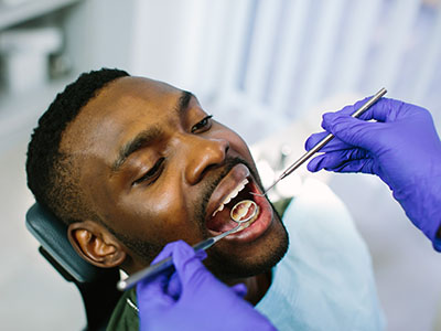 A man receiving dental care, with a dental hygienist performing the procedure, while he is seated in a dental chair.