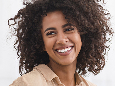 A woman with curly hair is smiling, looking slightly to her left.